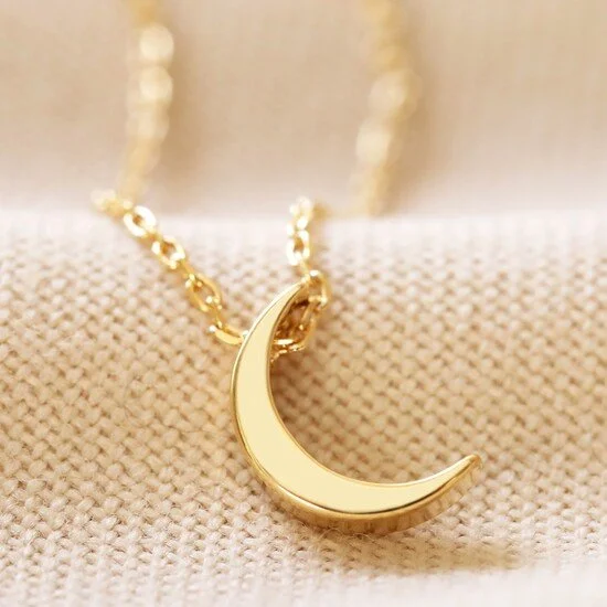A gold crescent moon pendant necklace resting on a textured fabric background.
