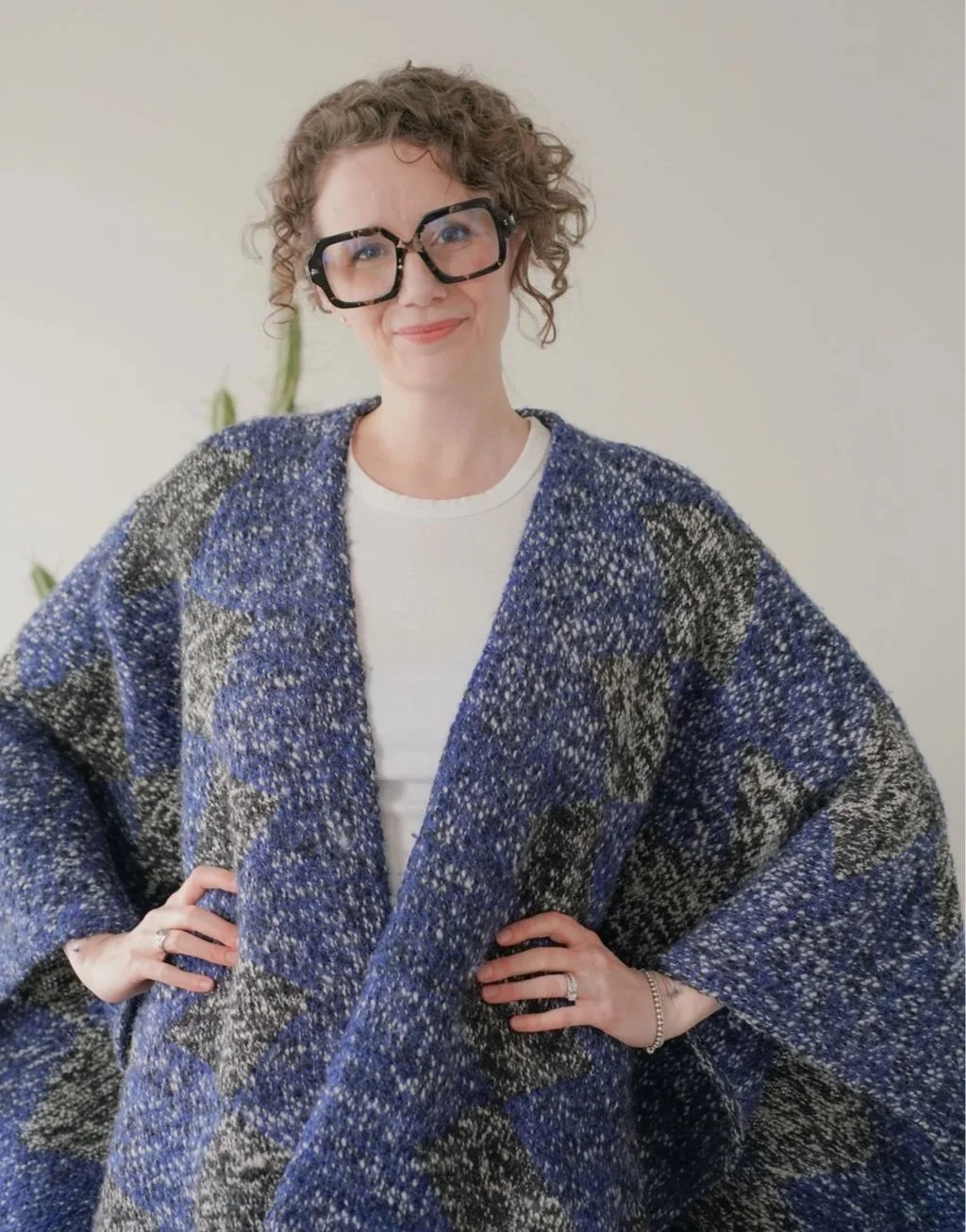 Meet Jessie - woman with curly hair and black glasses, smiling, wearing a blue patterned sweater over a white shirt.