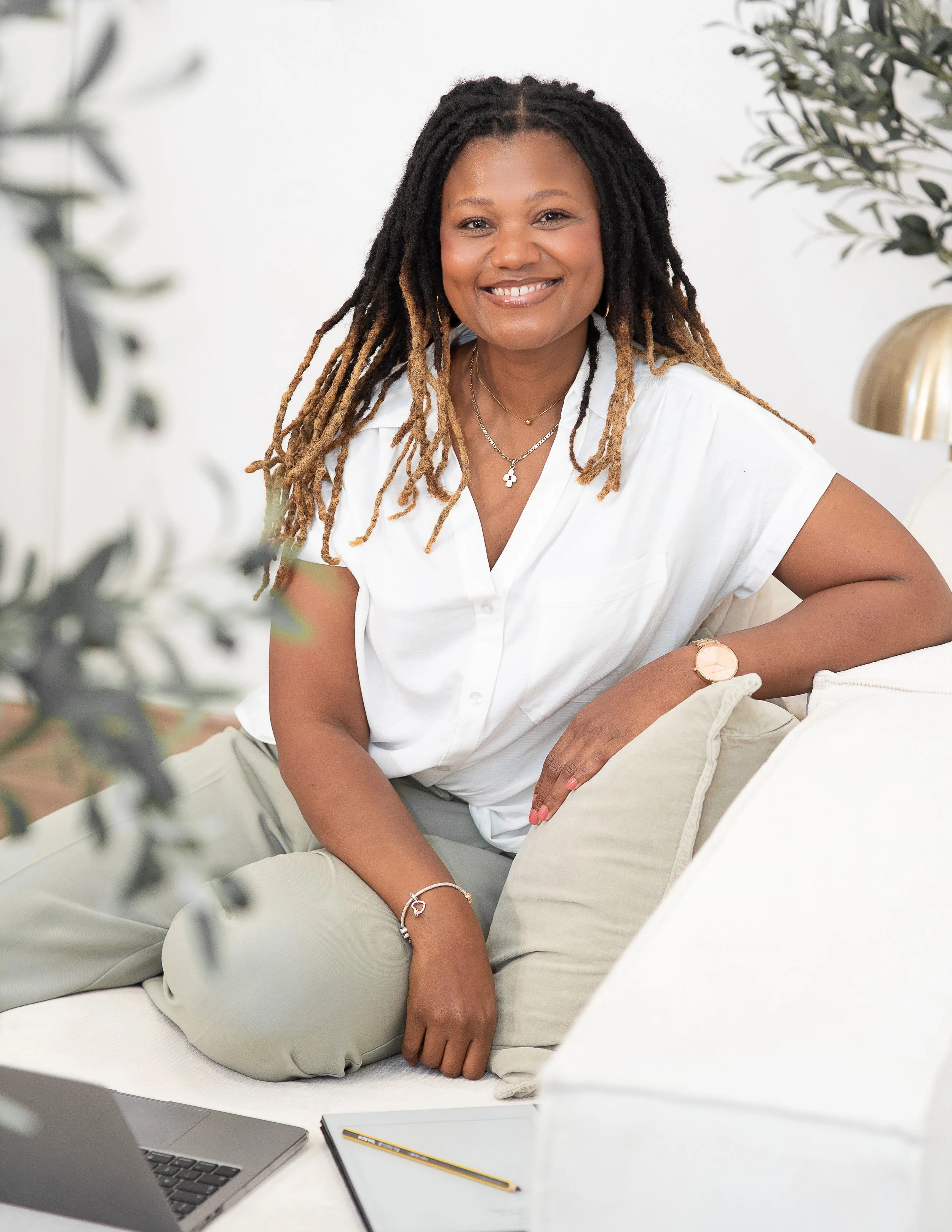 Natallie Ateere, founder of StandOut Leadership Consultancy, wearing a white shirt and sitting on a couch in a bright room with plants.