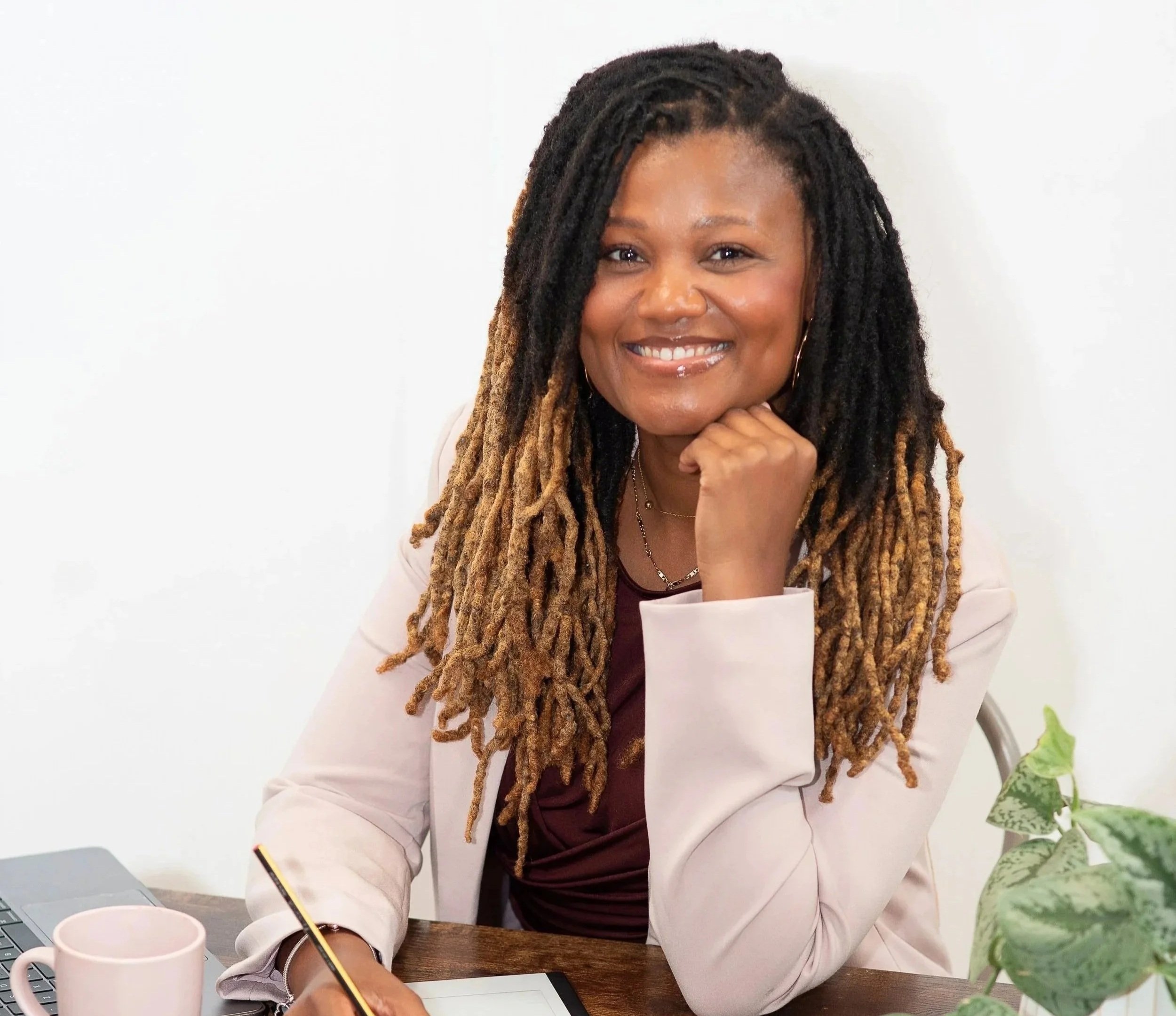HR professional and executive coach Natallie Ateere smiling at her desk with a notebook, coffee mug, and pen.