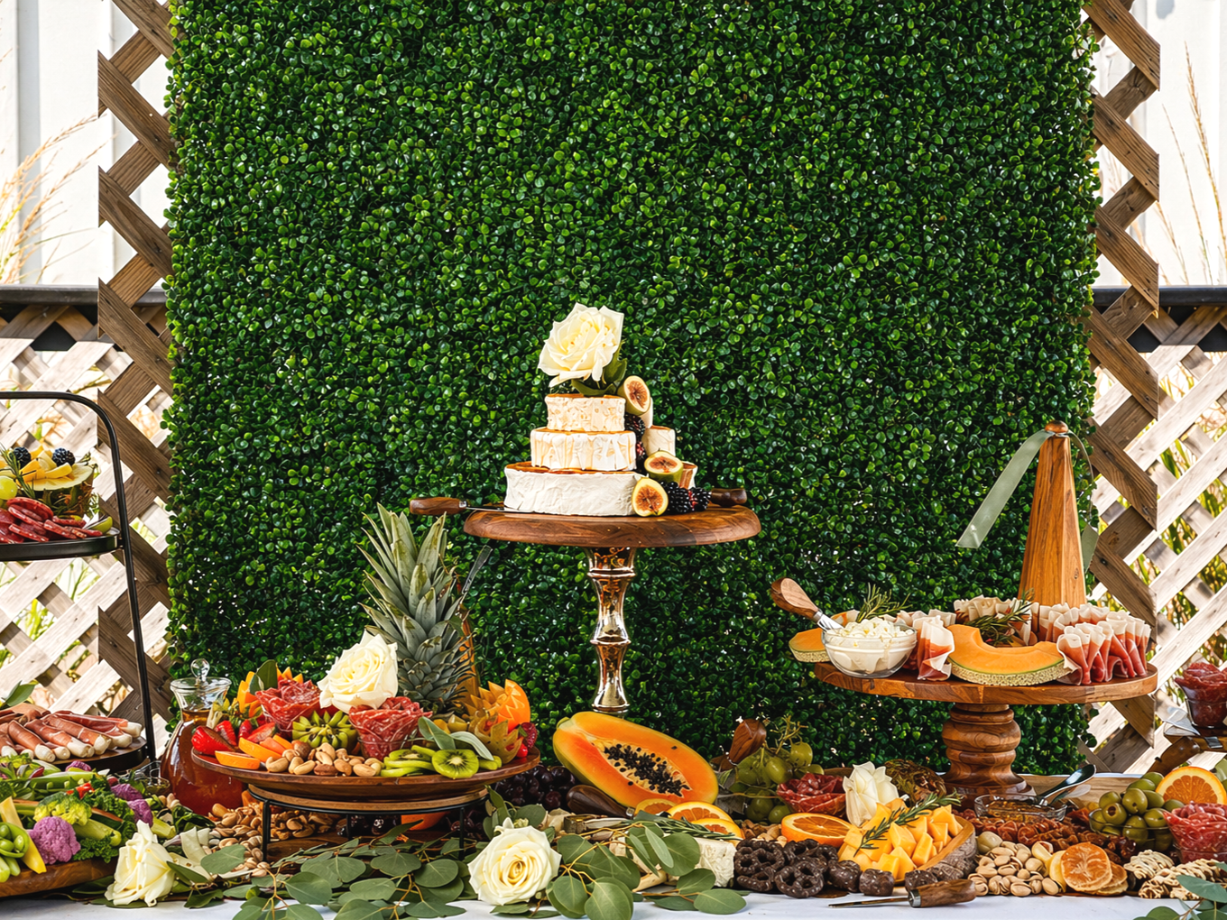A colorful outdoor buffet with a buffet of fruits, cheese, and charcuterie, with a greenery backdrop.
