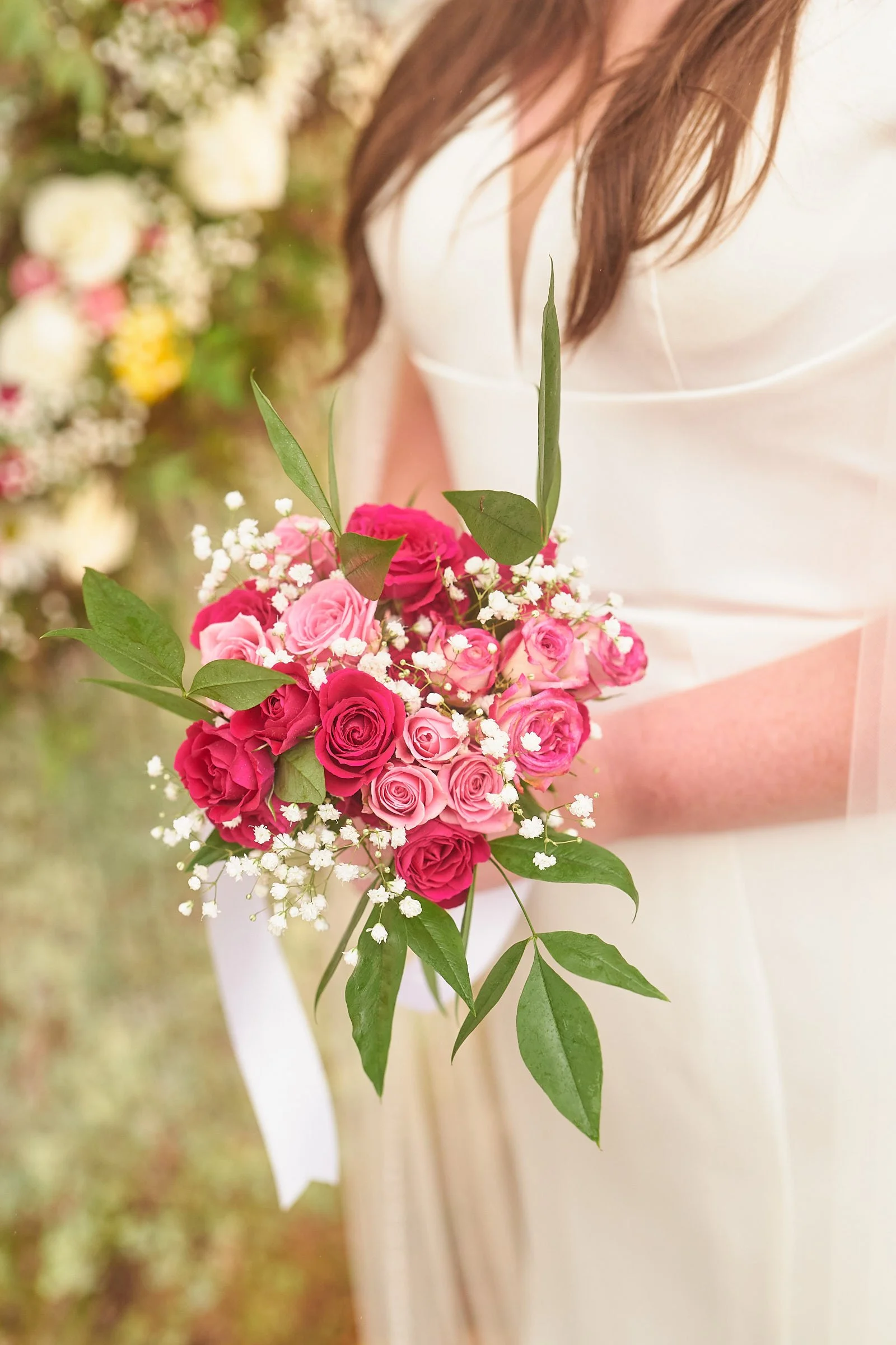 Close-up of a bride holding a bouquet of pink and white roses with green leaves during a wedding.