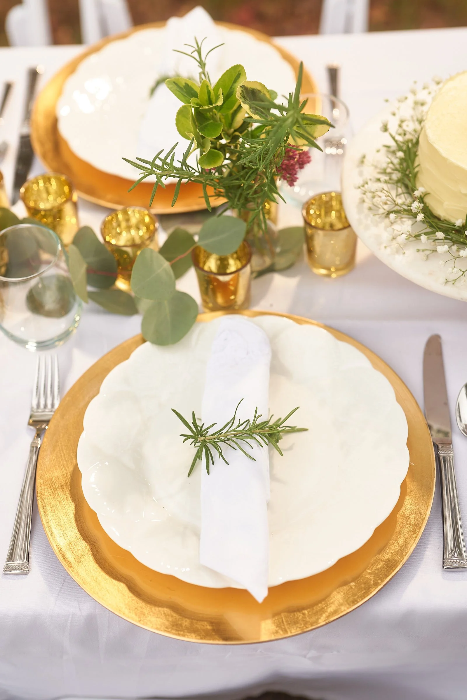A dessert on a gold-rimmed plate topped with a sprig of rosemary, served at a formal event with a white tablecloth and gold accents.