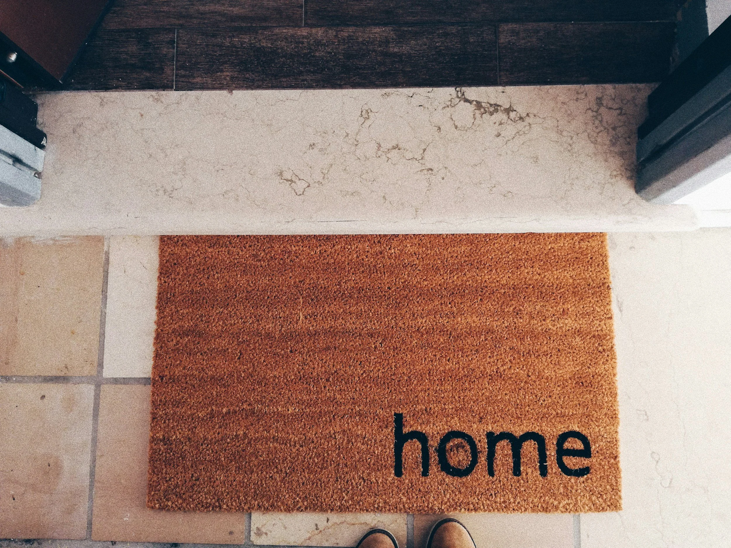Close-up of a textured doormat with the word 'welcome' printed on it, placed on a tiled floor, welcoming a mobile massage therapist.