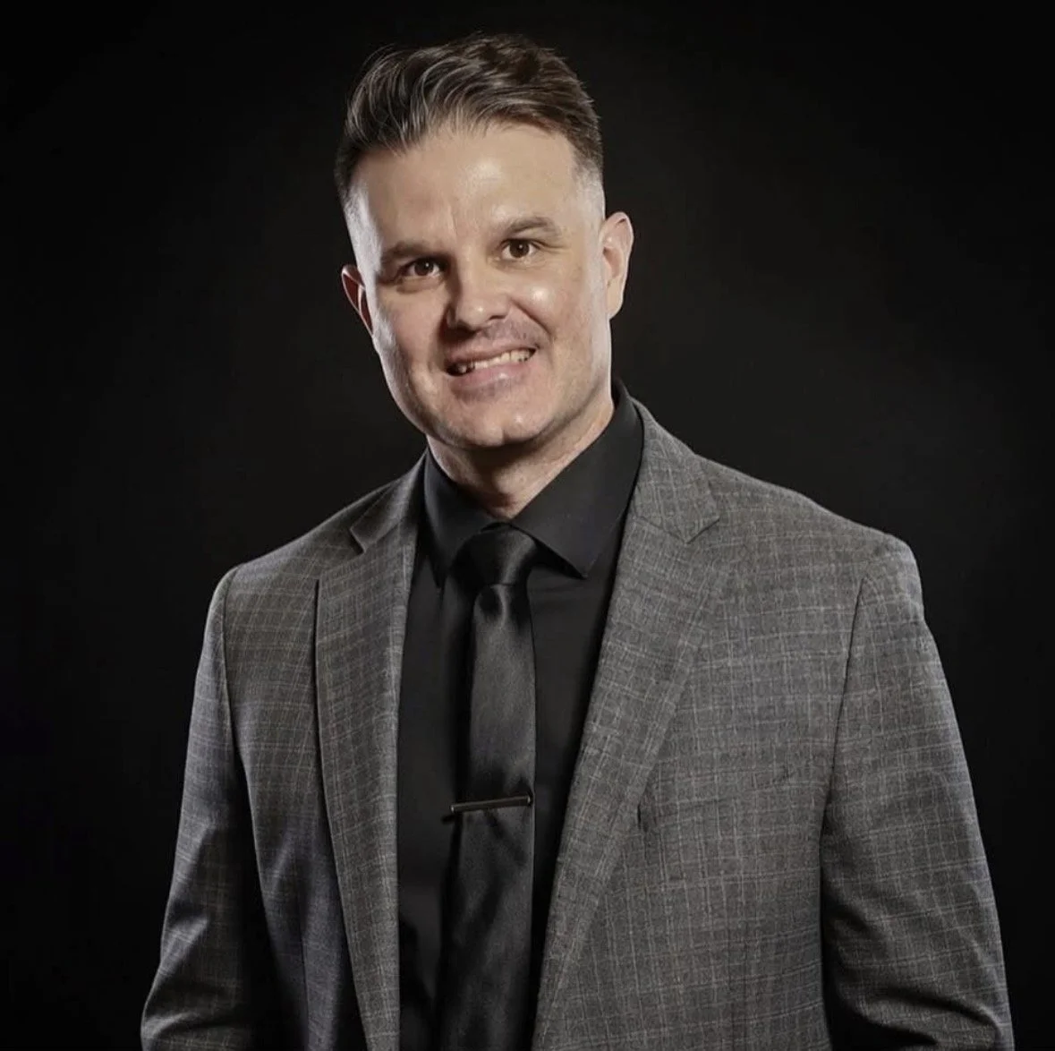 Portrait of Randy Jones, a licensed massage therapist, in a grey suit and black shirt with a black background.