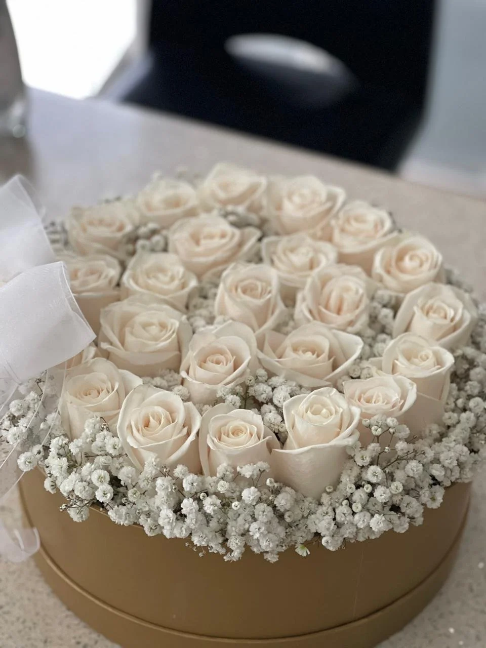 Un arreglo de rosas blancas y pequeñas flores blancas en una caja dorada.