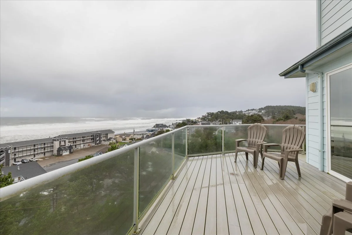 Ocean view from a balcony with two chairs, overcast sky, clouds and waves crashing on the shoreline.