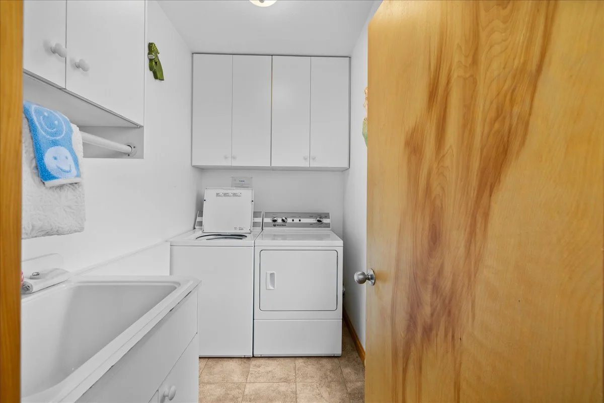 Laundry room with white washer and dryer, white cabinets, a utility sink, and a wooden door.