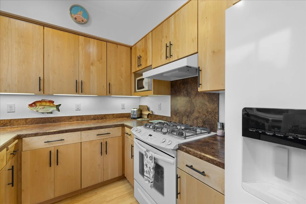 Kitchen with light wood cabinets, a gas stove, microwave, toaster, and a white refrigerator with a water and ice dispenser.