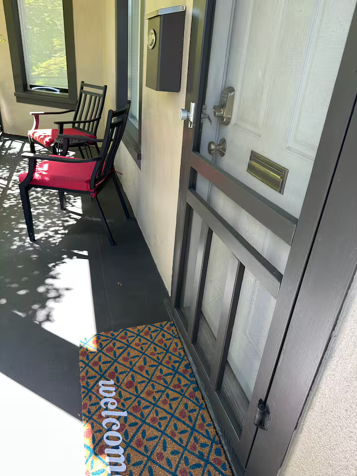 Front porch with chairs, welcome mat, and screen door.