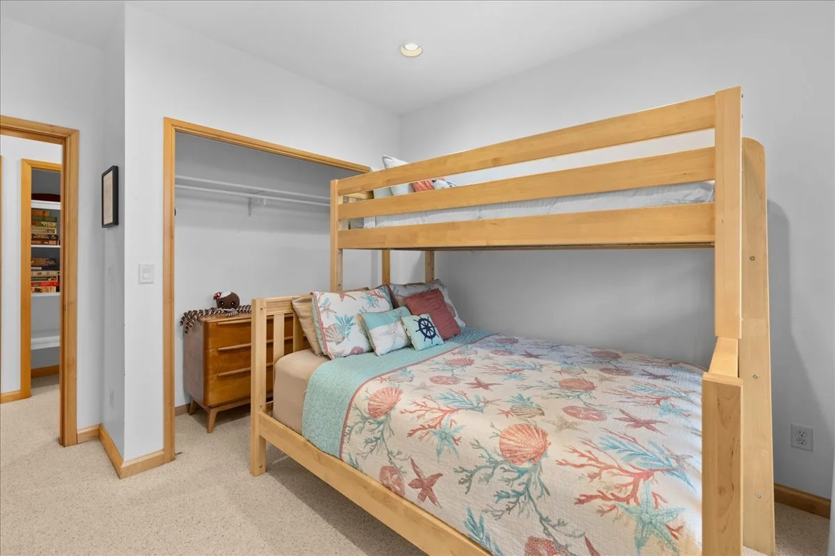 A bedroom with a wooden bunk bed, decorated with ocean-themed bedding and pillows, next to an open closet and a dresser.