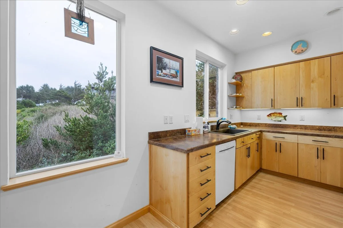 Kitchen with light wood cabinets, brown countertop, and a window showing greenery outside.