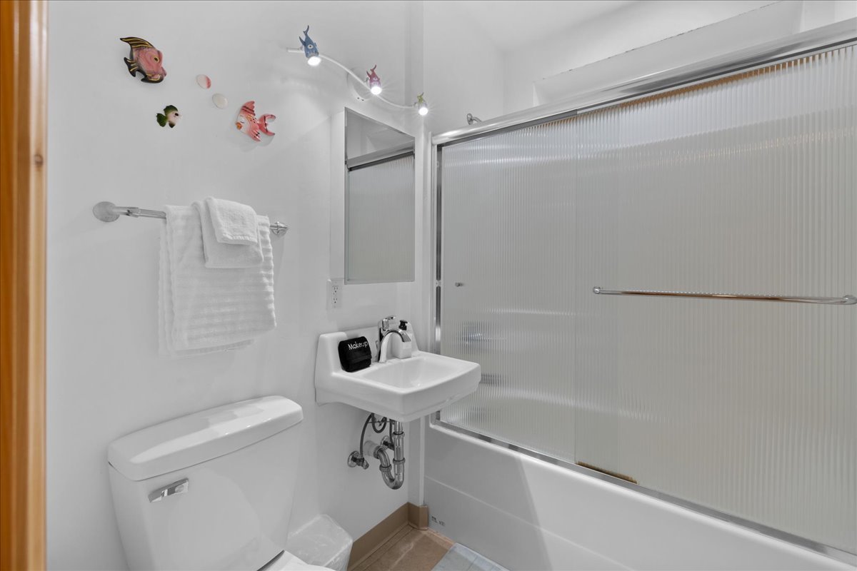 Small bathroom with white walls, fish-themed decor, a white towel on a metal bar, a small white sink, a toilet, and a frosted glass sliding shower door.