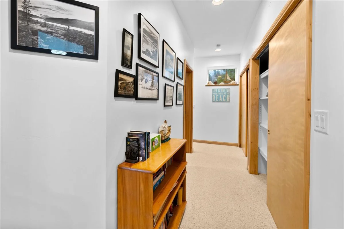 Hallway with framed pictures on the wall, a wooden bookshelf holding books and decorative items, a small window, and a sign that says "Life is better when you’re at the beach."