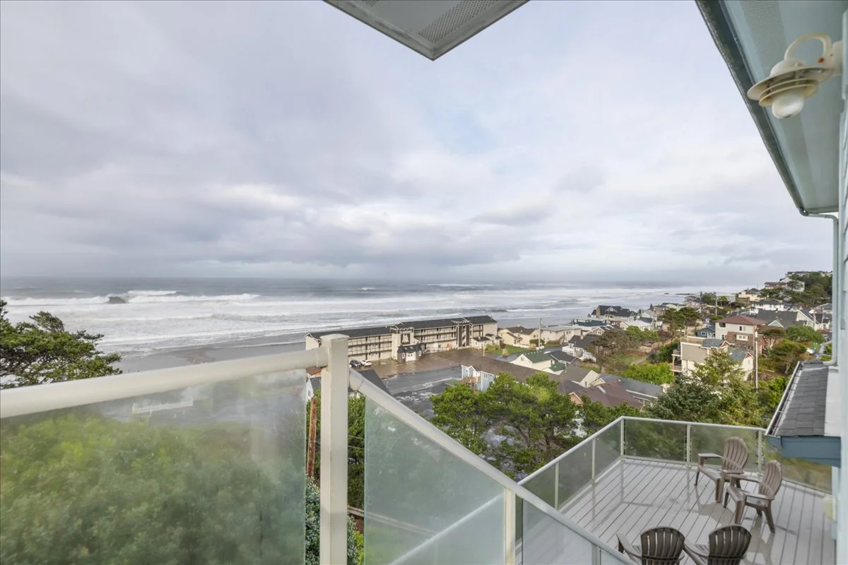 Balcony view overlooking a beach with waves, residential houses, and a cloudy sky.