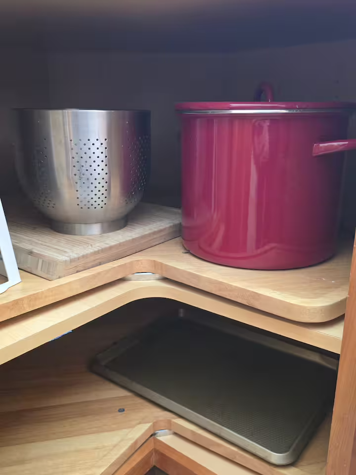 Countertop with a metal colander on a wooden cutting board and a red pot, with a black tray underneath.