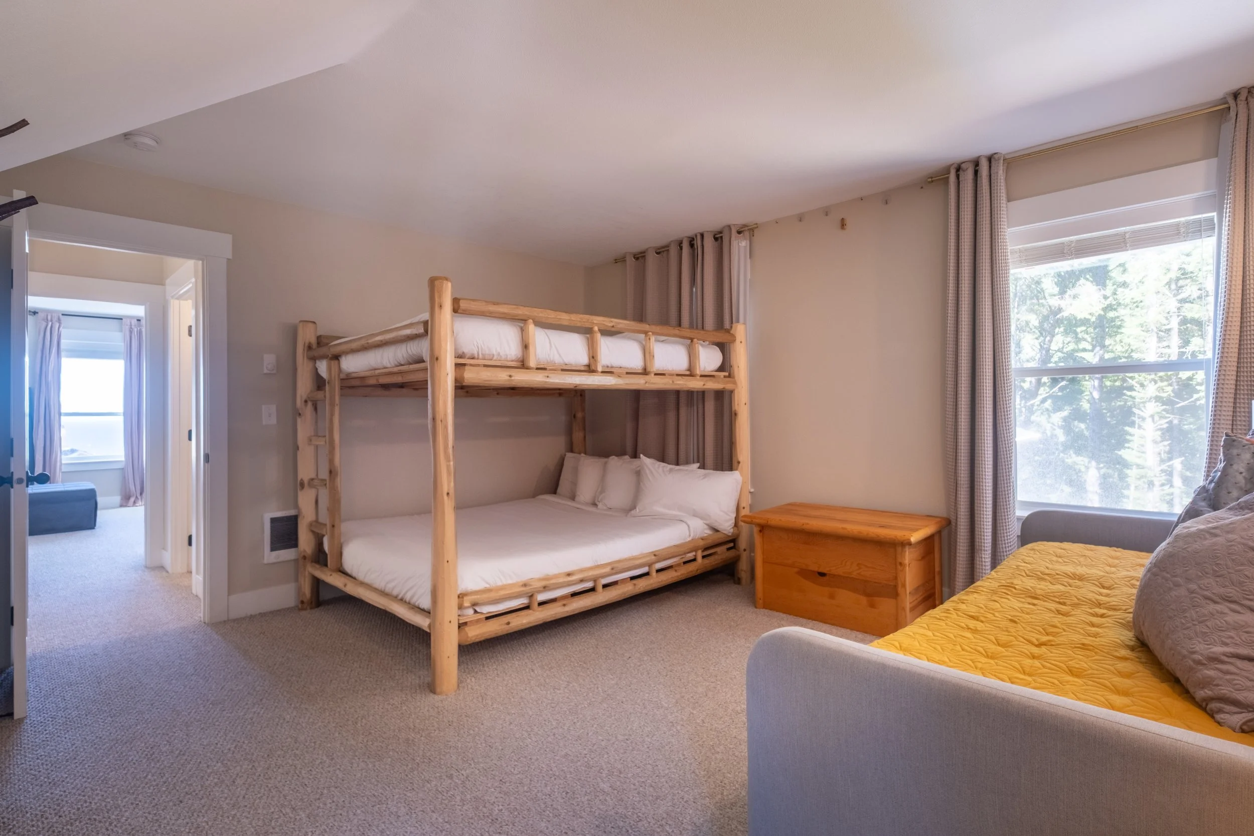 A bedroom with a wooden bunk bed, a window with curtains, and a bed with a yellow quilt.