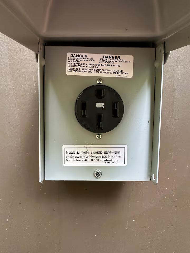 An electrical outlet inside a metal box mounted on a wall with warning labels.