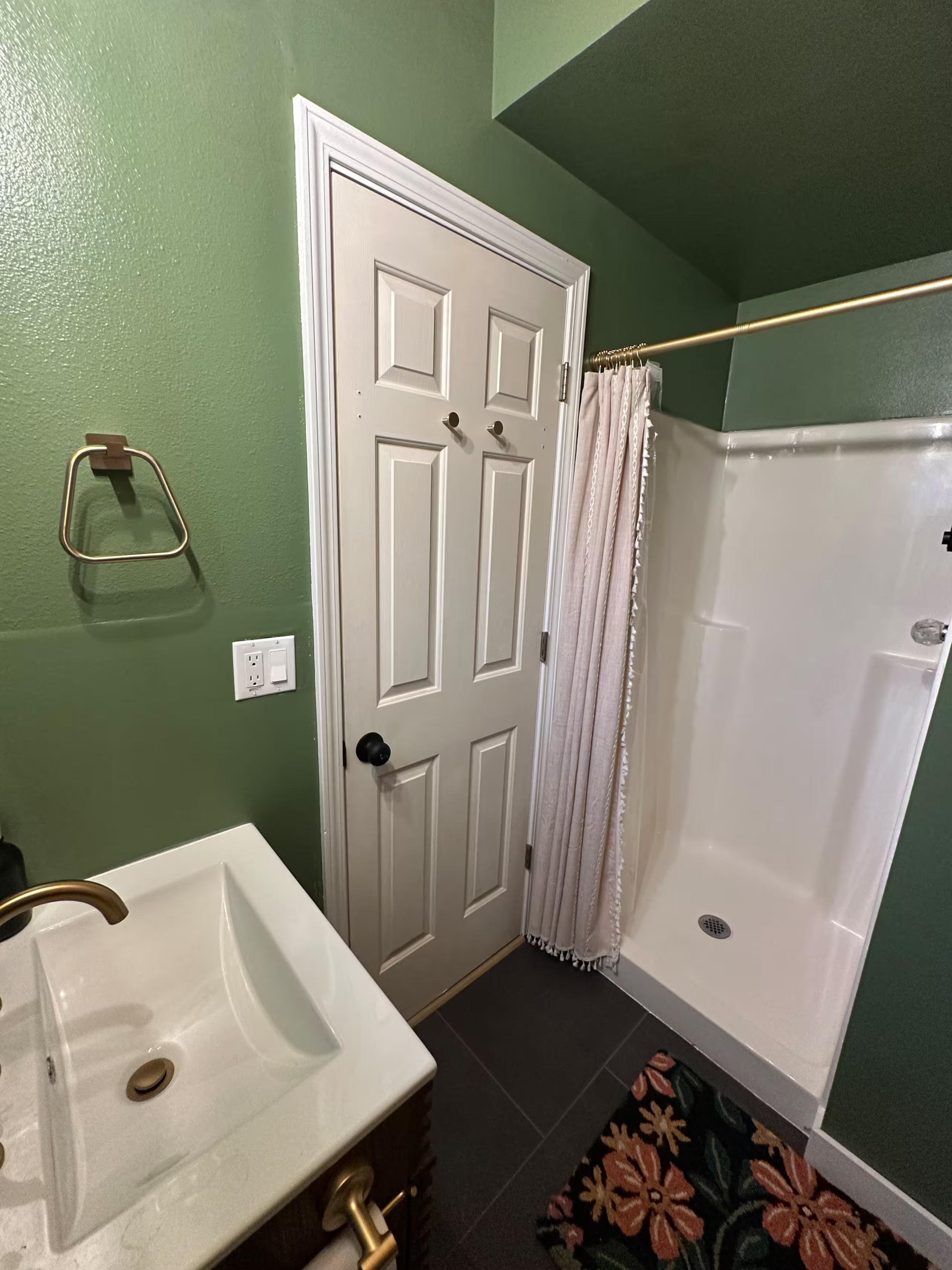 Bathroom with green walls, white door, beige shower curtain, white sink, and black tile flooring.