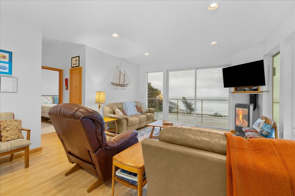 Living room with beige and brown furniture, a large flat-screen TV, a fireplace, sliding glass doors to a balcony, and nautical decor.