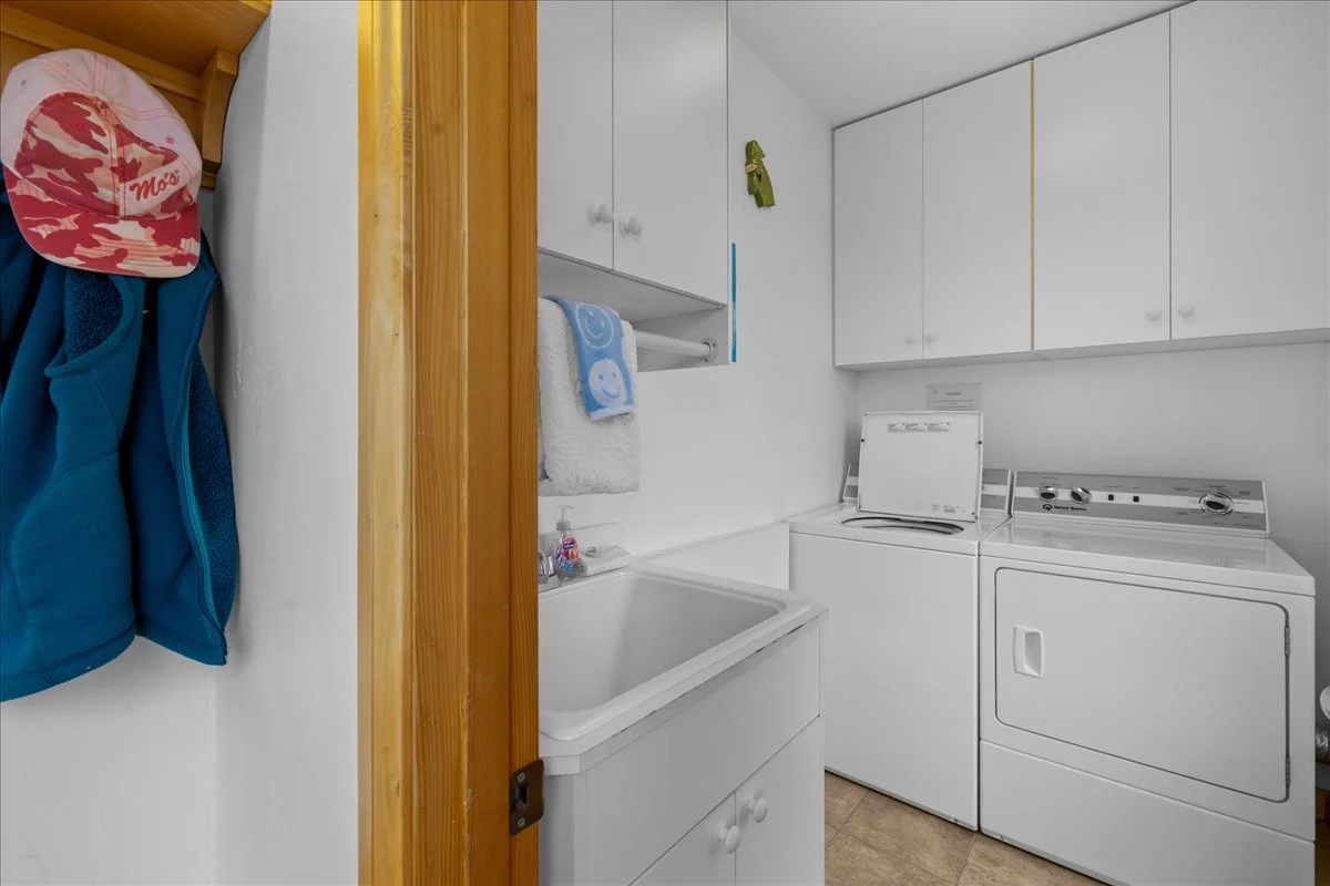 Laundry room with white cabinets, a washing machine, a dryer, a utility sink, and hanging towels and jackets.