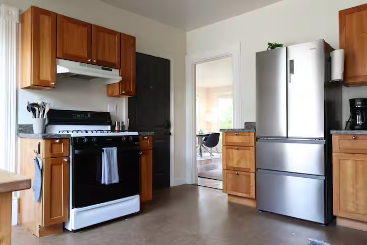 Kitchen with wooden cabinets, black gas stove, stainless steel refrigerator, and black coffee maker.