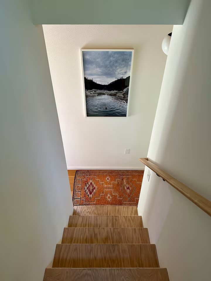 View looking down a staircase into a small landing area with a colorful patterned rug and a nature photograph on the wall.