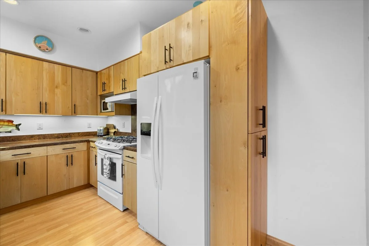Kitchen with wooden cabinets, a white refrigerator, a white stove, and brown countertops. There are small appliances on the counter and a fish-shaped sculpture on the wall.