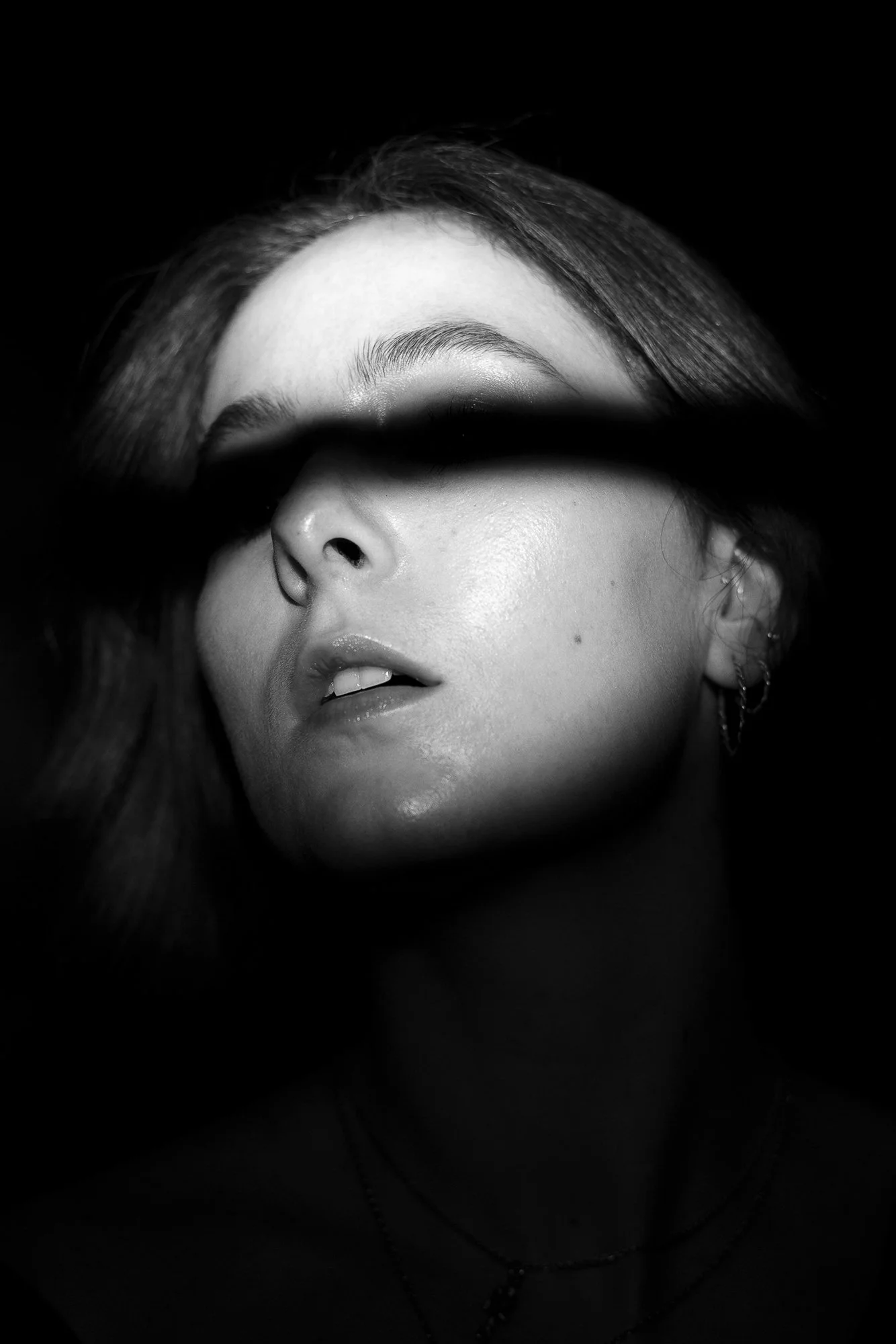 Black-and-white close-up photo of a woman's face, focusing on her lips, nose, and eyebrows, partially obscured by darkness.