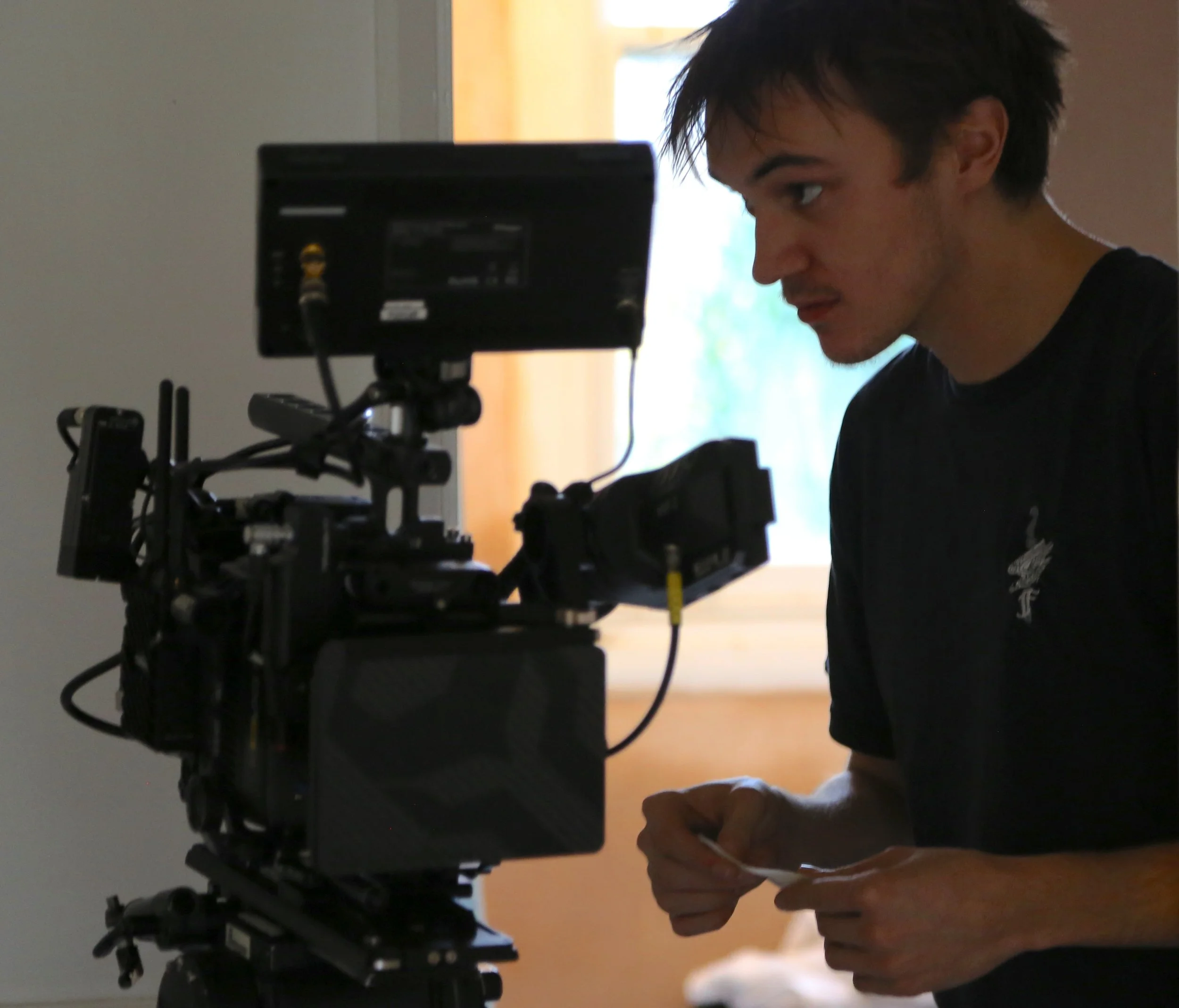 Person looking at a camera mounted on a tripod, with a window in the background.
