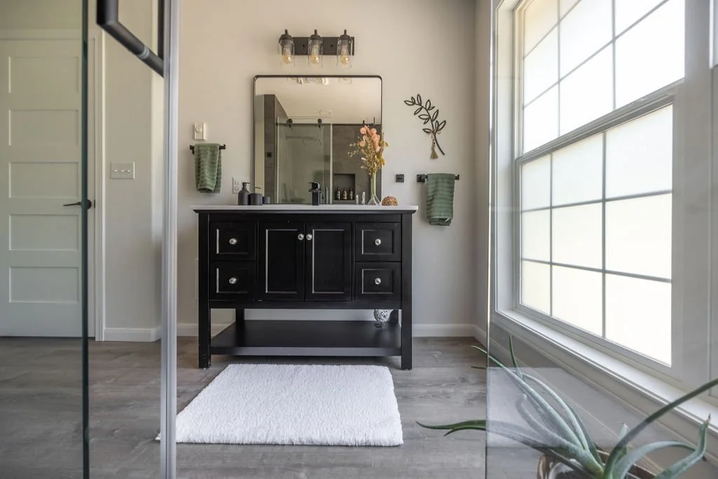 bathroom remodel showing floor to ceiling window with natural light, free-standing black and white vanity, and living plants
