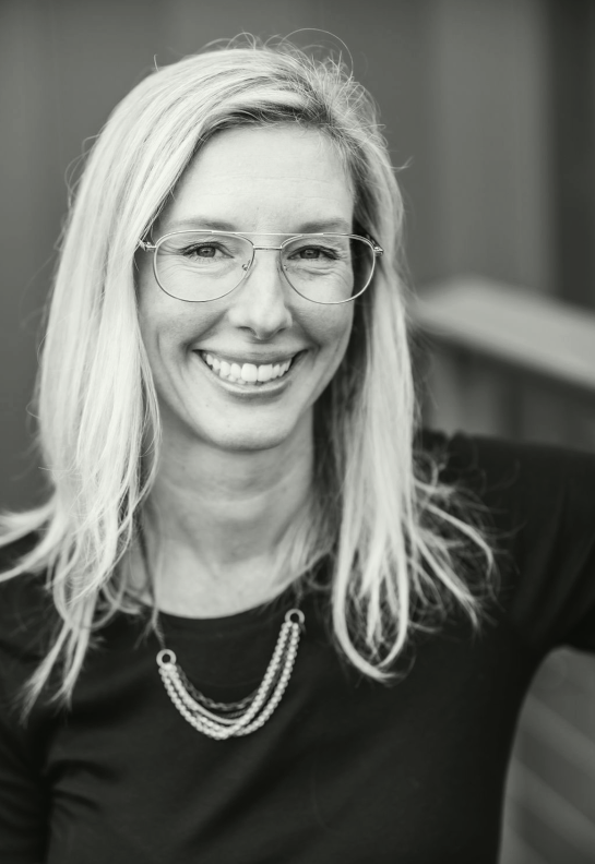 Black and white photo of Studio Nosylla's founder, Allyson Strowbridge, wearing glasses, shoulder-length blonde hair, wearing a black top and layered necklaces.