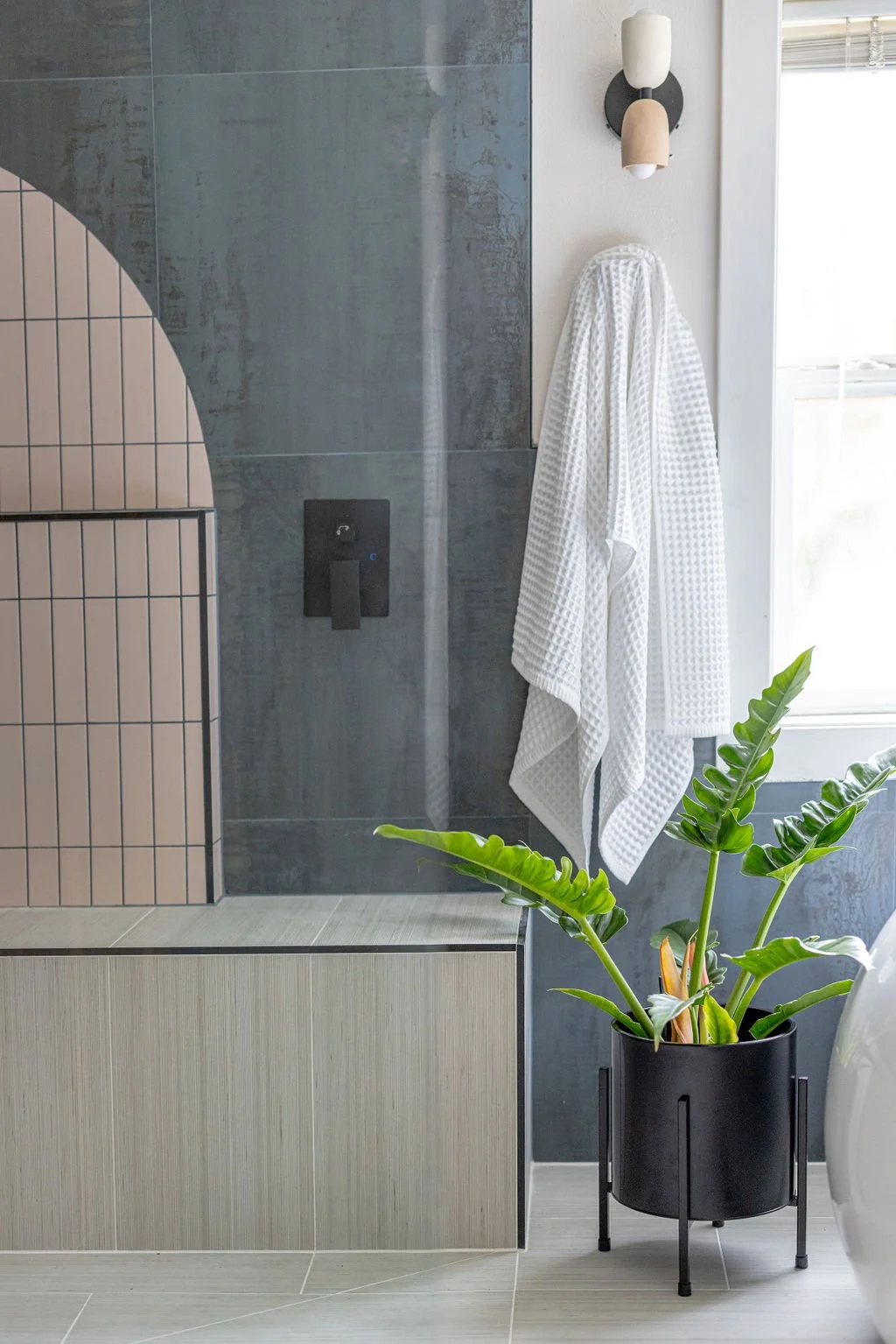 Bathroom walk-in shower with plants, colorful unique tile install pattern, and unique wall sconce lighting