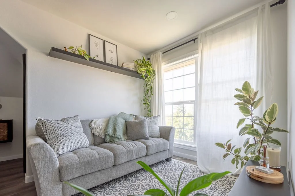 guest loft sitting area near large floor to ceiling window with living plants, grey sofa and neutral monochromatic decor