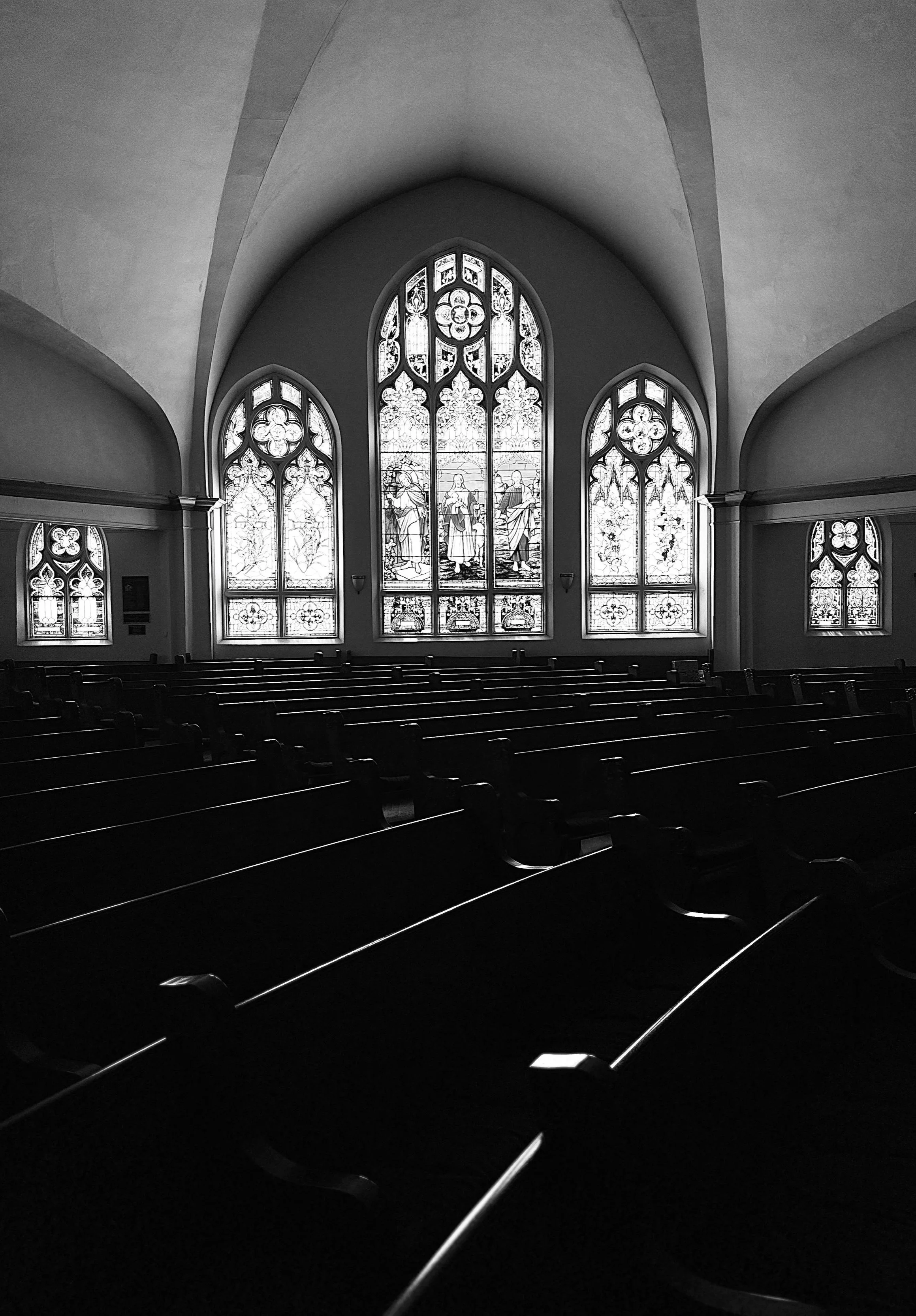 Interior of a church with multiple stained glass windows, wooden pews, and a vaulted ceiling.
