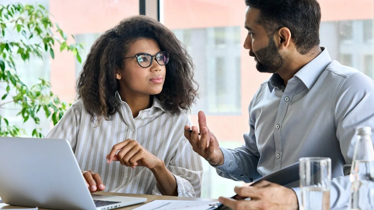 Three people engaged in a discussion, looking at documents or notes, in an office setting.