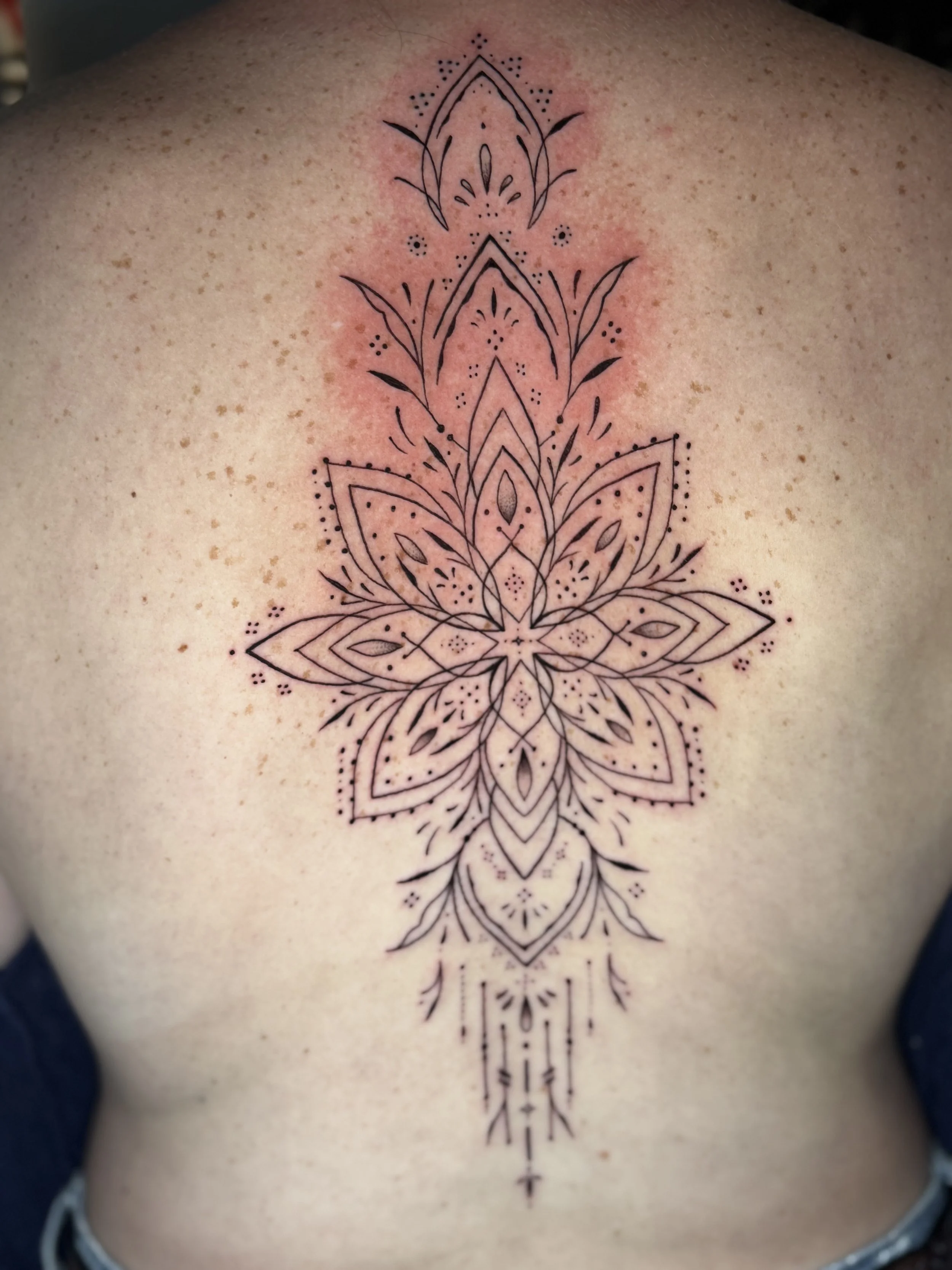 A black line tattoo in geometric and floral style on a person's chest, centered vertically, with some redness around the area.