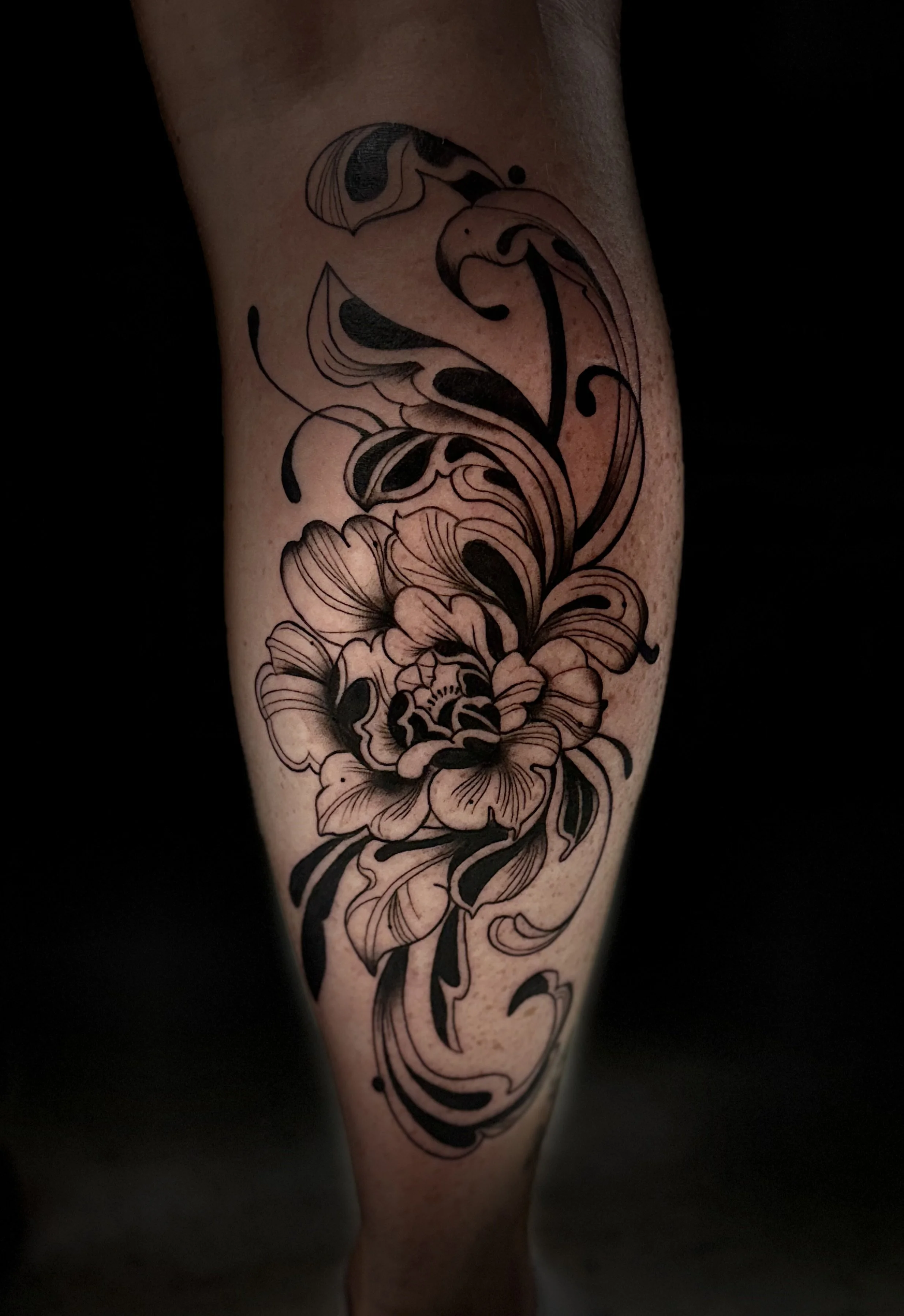 A black and white tattoo of a floral design with swirling lines and petals on a person's arm.