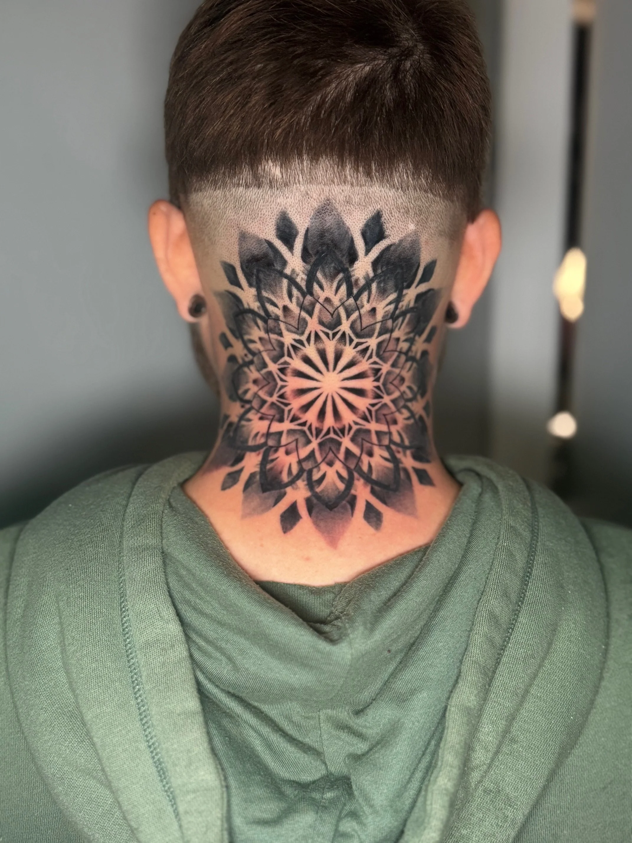 Back of a person's head with a shaved head tattoo featuring a geometric floral pattern on the neck.