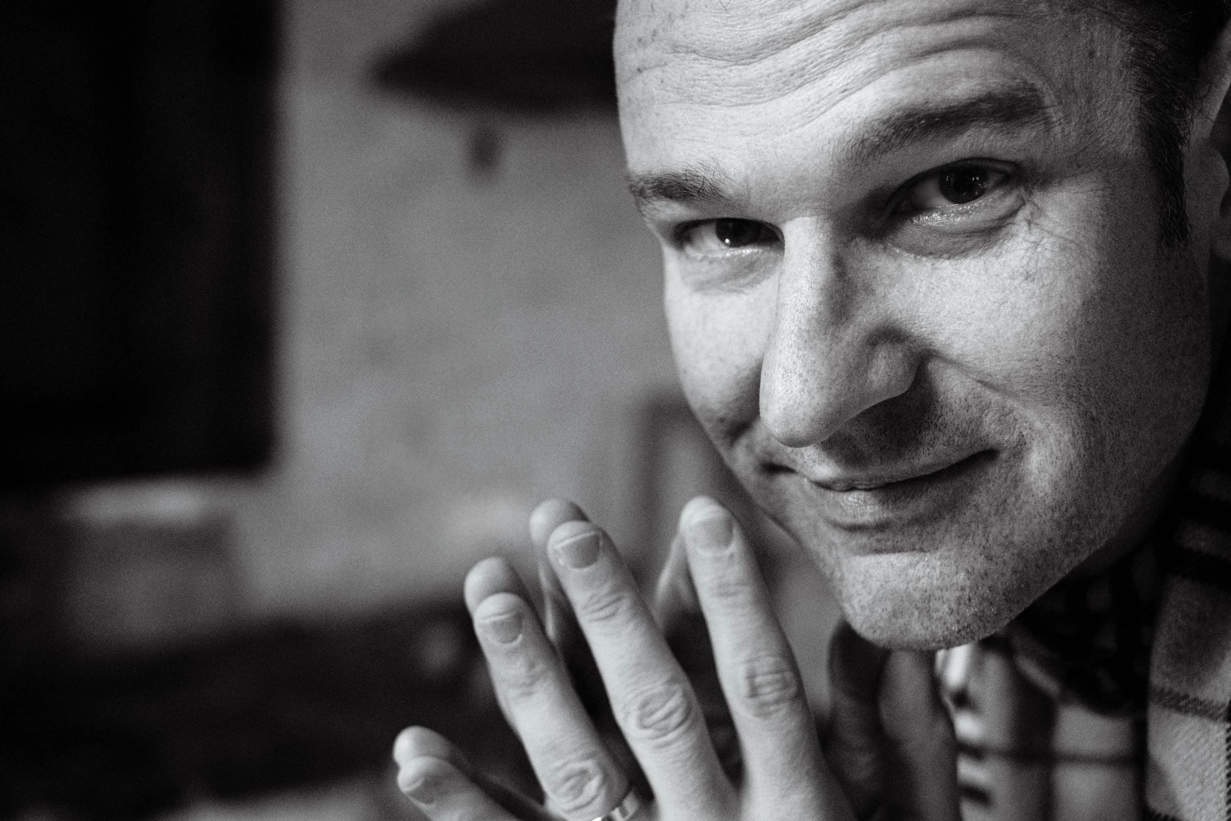 Close-up of a man's face, smiling and looking at a handheld device, black and white photo.