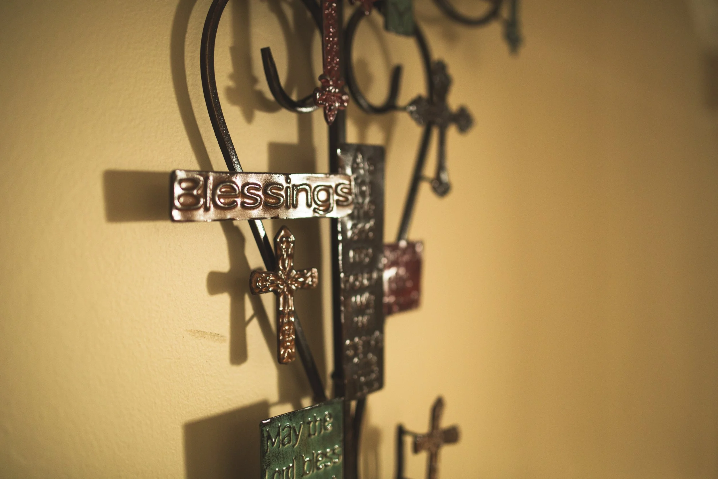 Wall-mounted decorative metal keys and keychains with engraved or embossed tags and symbols, some with words like 'Blessings' and dates, hanging in a row.