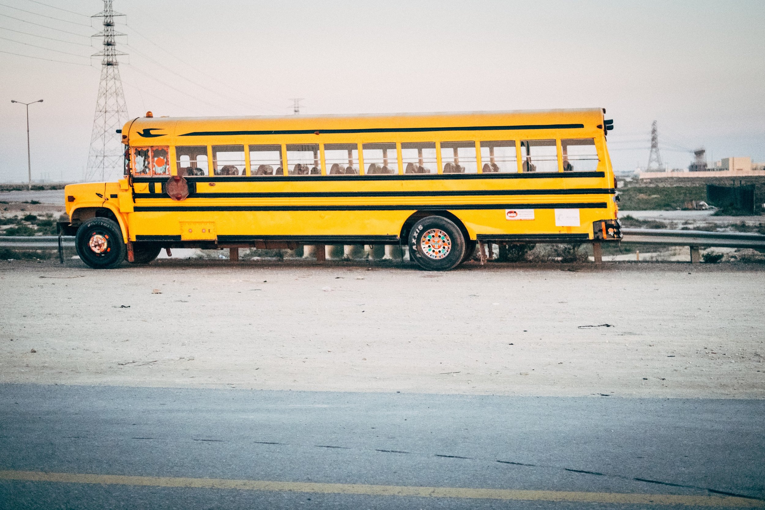 Yellow school bus parked on the side of an empty road with power lines and industrial buildings in the background.