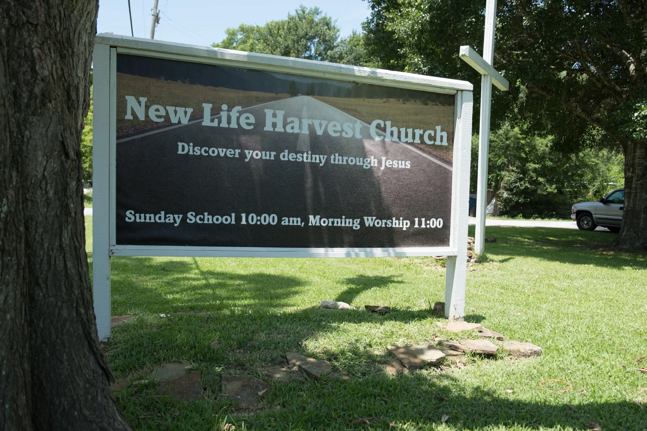 Sign for New Life Harvest Church with service times, surrounded by trees and grass in an outdoor setting.