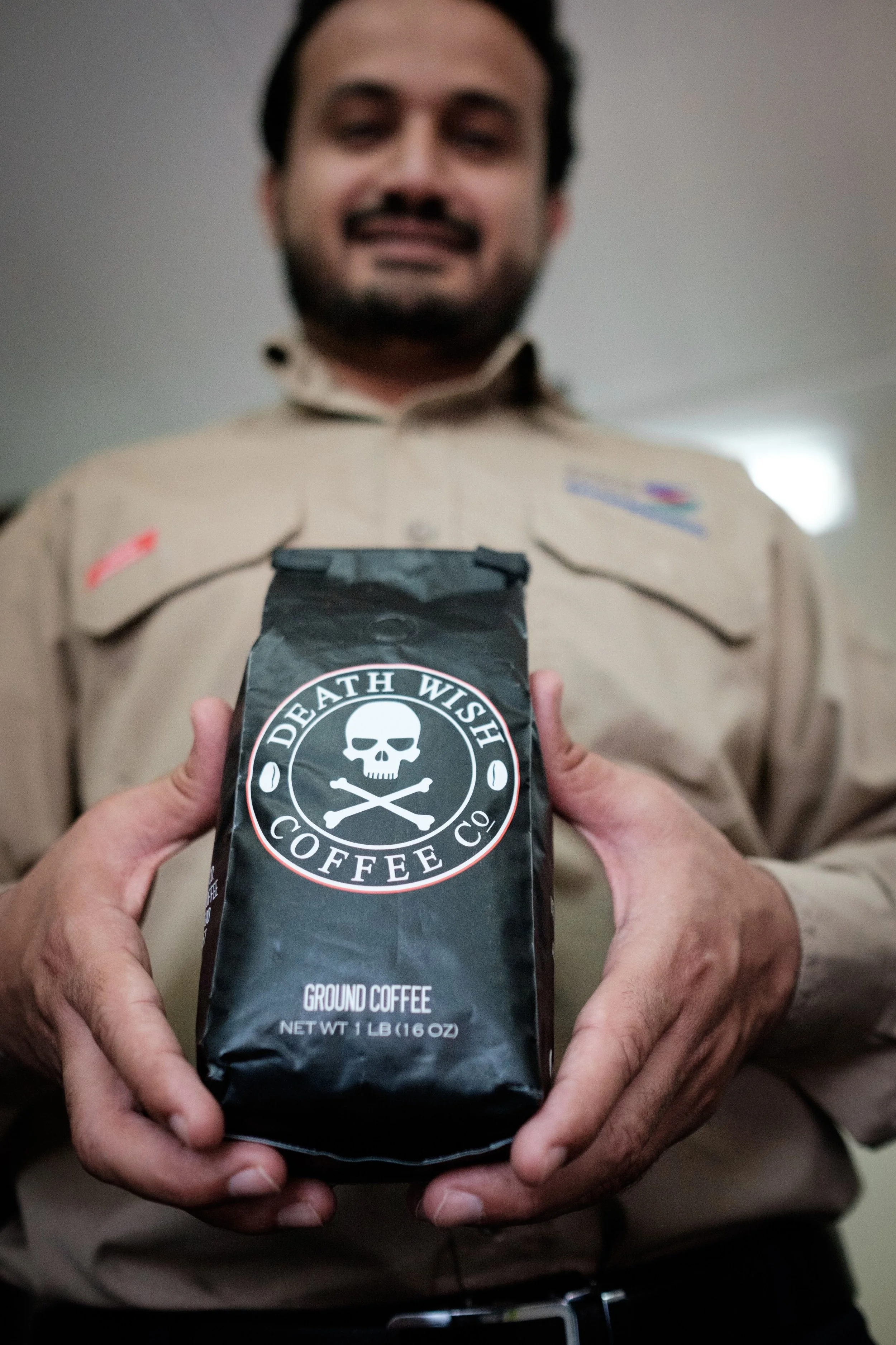 A person with a goatee and dark hair holding a 1-pound bag of Death Wish Coffee Ground Coffee with both hands.