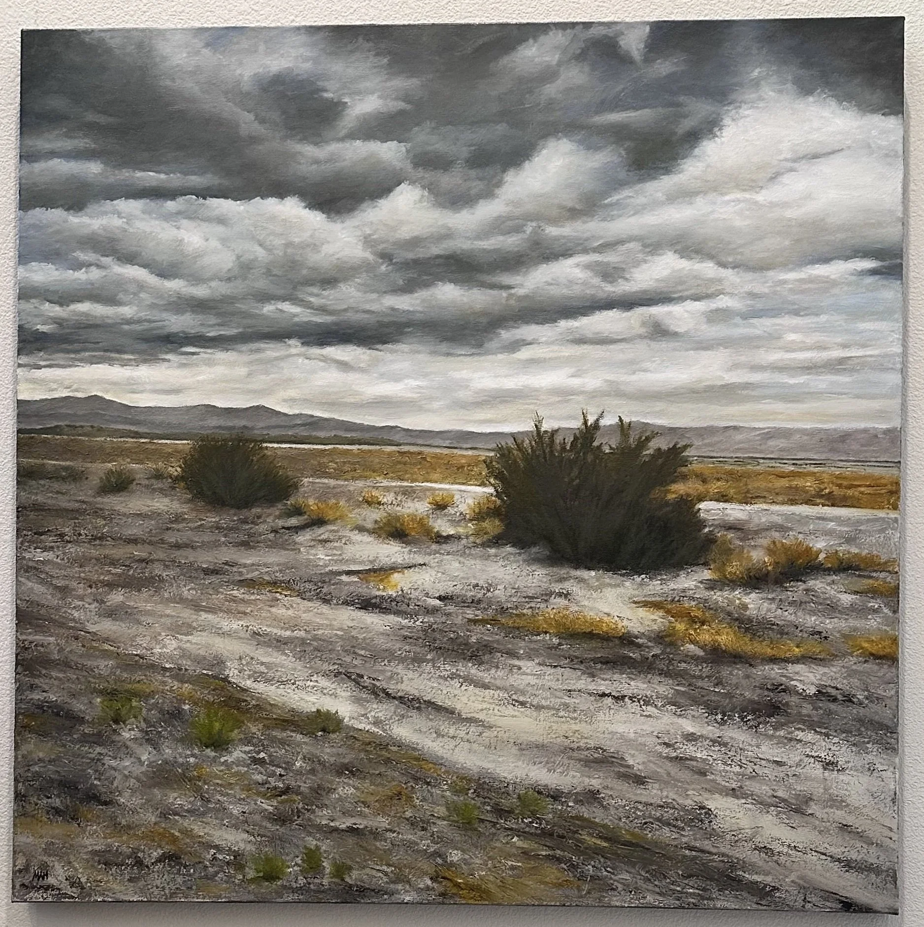 Contemporary cloudscape oil painting ‘Solace Amidst Storm’ by Michael A Hidalgo, dramatic skies, atmospheric clouds, peaceful light over open desert landscape, sparse bushes, mountain range. Fine art, luxury interior, see at MAHStudio.net