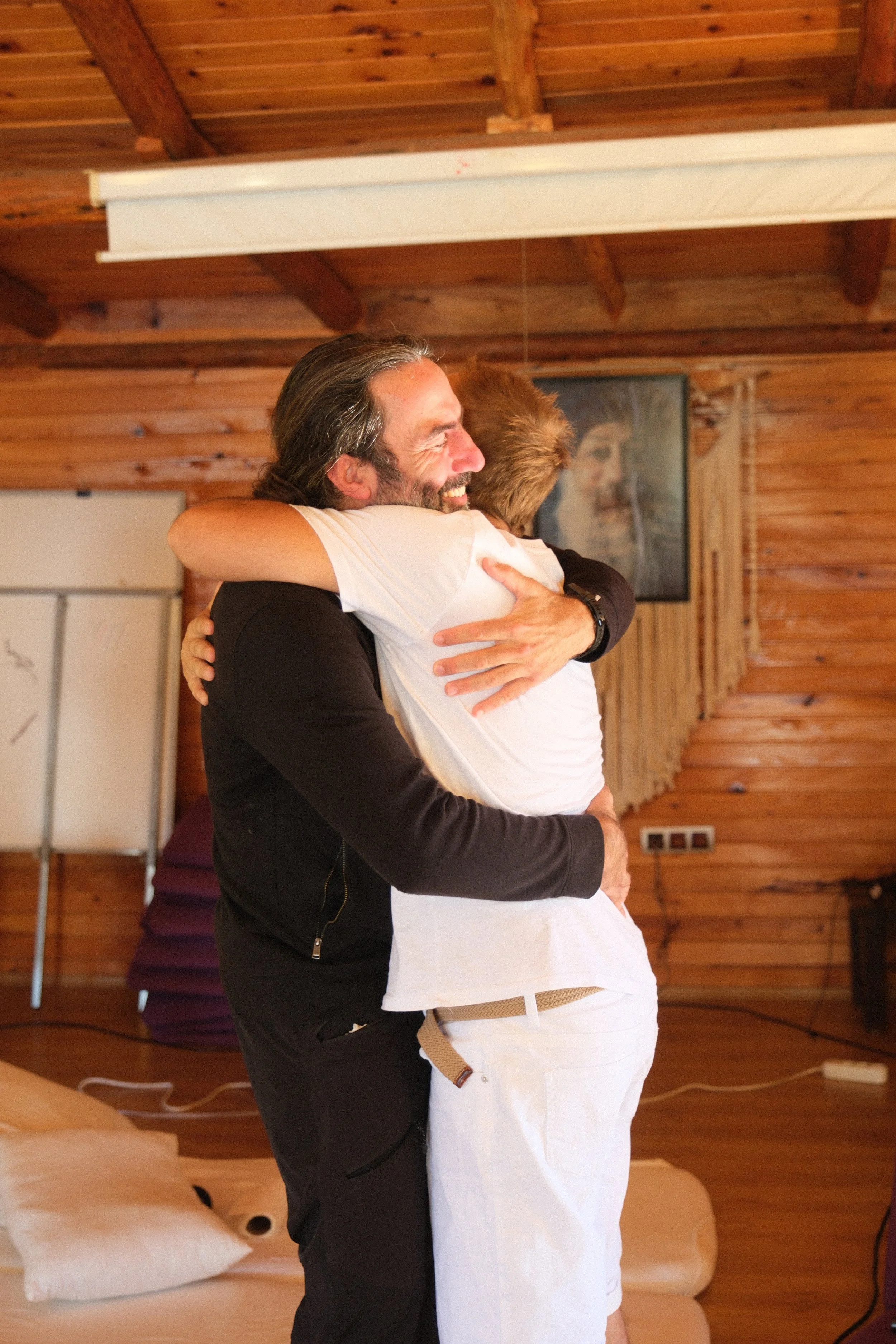 Two men hugging each other in a room Osho celebration, evening meeting, diamond breath school.