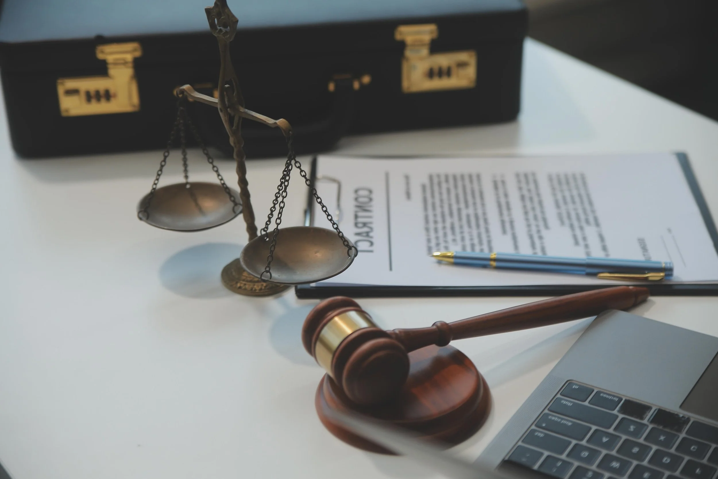 A desk scene with a small scale of justice, a gavel, a document titled 'LEGAL ACCEPTANCE,' a pen, and a laptop keyboard visible.
