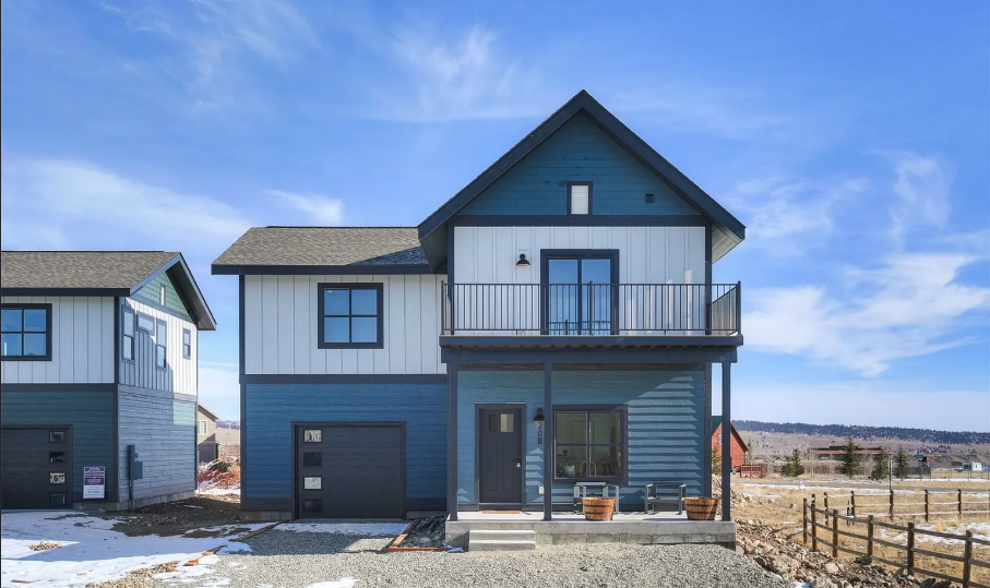 A modern modular single family home by Fading West featuring a small front porch and balcony under a blue sky with some clouds.