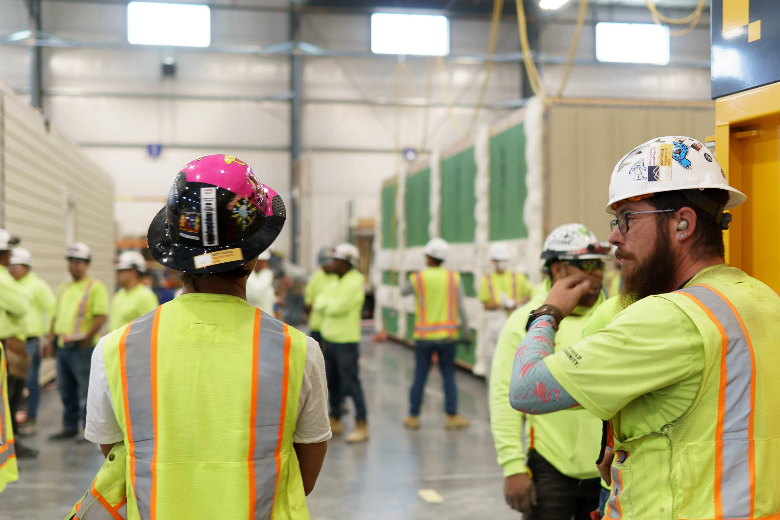 Group of people wearing safety vests and helmets inside an Fading West's manufacturing facility.