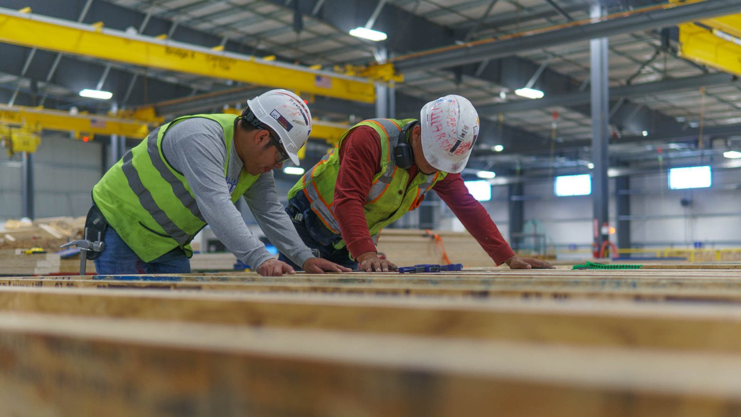 Two construction workers wearing hard hats and safety vests working on a lumber project inside the Fading West Factory in Buena, Vista CO